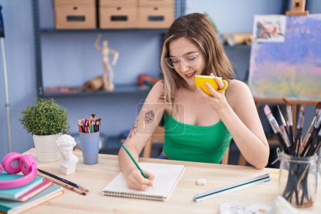 Téléchargez les photos : Young woman artist drawing on notebook drinking coffee at art studio - en image libre de droit