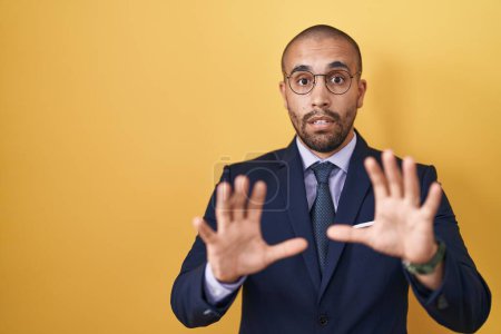 Photo for Hispanic man with beard wearing suit and tie afraid and terrified with fear expression stop gesture with hands, shouting in shock. panic concept. - Royalty Free Image