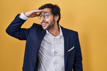 Photo for Handsome latin man standing over yellow background very happy and smiling looking far away with hand over head. searching concept. - Royalty Free Image