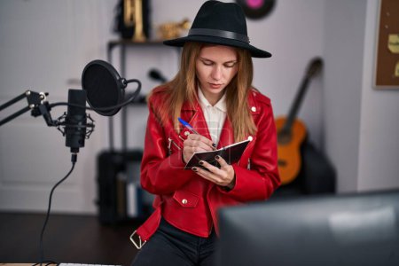 Téléchargez les photos : Jeune femme blonde musicienne écrivant sur carnet au studio de musique - en image libre de droit