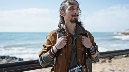Téléchargez les photos : Jeune homme hispanique touriste portant un sac à dos au bord de la mer - en image libre de droit