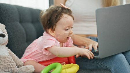 Photo for Mother and daughter using laptop while playing with hoops at home - Royalty Free Image