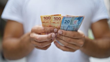 Junger hispanischer Mann zählt mexikanische Pesos auf der Straße