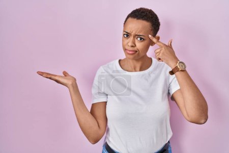 Photo for Beautiful african american woman standing over pink background confused and annoyed with open palm showing copy space and pointing finger to forehead. think about it. - Royalty Free Image