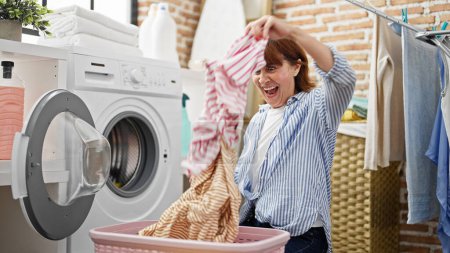 Photo for Middle age woman throwing clothes on air at laundry room - Royalty Free Image
