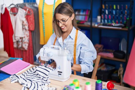 Téléchargez les photos : Jeune belle femme hispanique tailleur souriant confiant en utilisant une machine à coudre à l'usine de vêtements - en image libre de droit