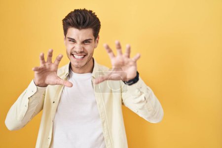 Photo for Young hispanic man standing over yellow background smiling funny doing claw gesture as cat, aggressive and sexy expression - Royalty Free Image