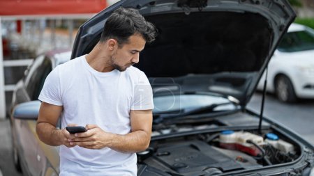 Téléchargez les photos : Jeune homme hispanique texto à l'assurance pour panne de voiture à la rue - en image libre de droit
