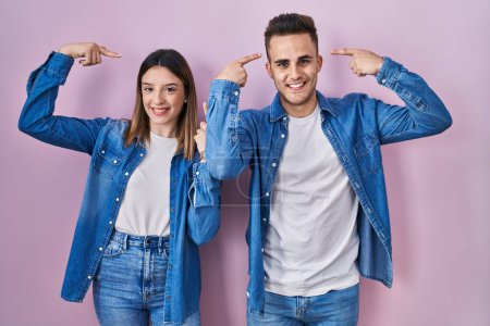 Photo for Young hispanic couple standing over pink background smiling pointing to head with both hands finger, great idea or thought, good memory - Royalty Free Image