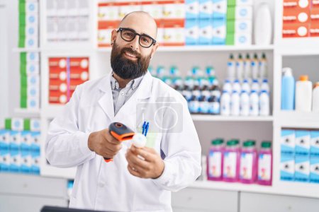 Foto de Joven hombre calvo farmacéutico escaneo píldoras botella en la farmacia - Imagen libre de derechos