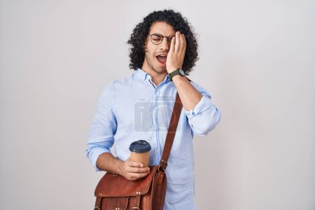 Foto de Hombre hispano con el pelo rizado bebiendo una taza de café para llevar bostezando cansado cubriendo media cara, ojos y boca con la mano. cara duele en el dolor. - Imagen libre de derechos