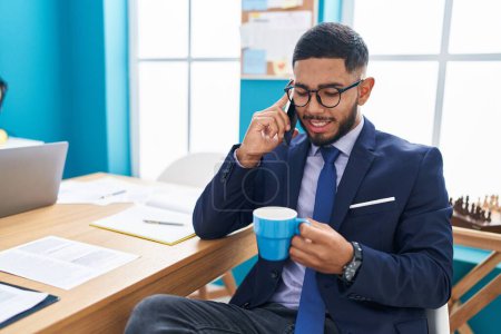 Photo for Young latin man business worker talking on smartphone drinking coffee at office - Royalty Free Image