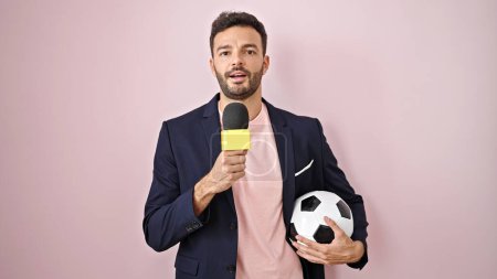 Téléchargez les photos : Jeune homme hispanique journaliste de football faisant une interview parlant sur fond rose isolé - en image libre de droit
