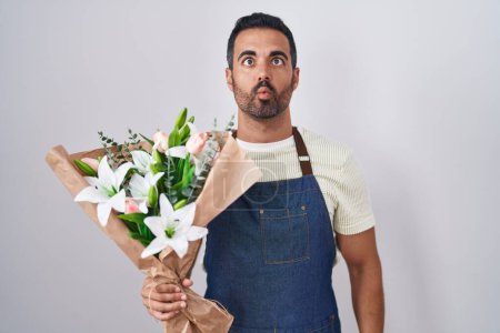 Photo for Hispanic man with beard working as florist making fish face with lips, crazy and comical gesture. funny expression. - Royalty Free Image