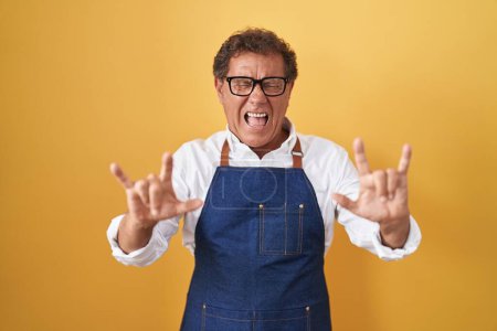 Photo for Middle age hispanic man wearing professional cook apron shouting with crazy expression doing rock symbol with hands up. music star. heavy concept. - Royalty Free Image