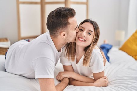 Photo for Man and woman couple lying on bed hugging each other and kissing at bedroom - Royalty Free Image