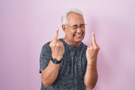 Foto de Middle age man with grey hair standing over pink background showing middle finger doing fuck you bad expression, provocation and rude attitude. screaming excited - Imagen libre de derechos