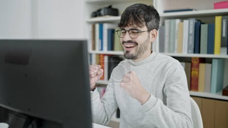 Téléchargez les photos : Jeune homme hispanique utilisant un ordinateur portable célébrant à l'université salle de classe - en image libre de droit