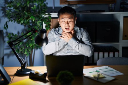 Téléchargez les photos : Jeune homme chinois travaillant à l'aide d'un ordinateur portable la nuit criant et étouffant parce que l'étranglement douloureux. problème de santé. concept d'asphyxie et de suicide. - en image libre de droit