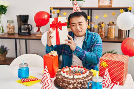 Foto de Young chinese man celebrating birthday holding gift at home - Imagen libre de derechos