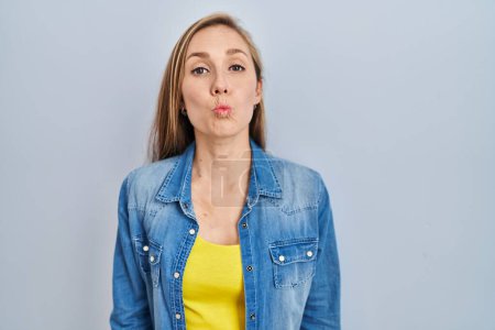 Photo for Young blonde woman standing over blue background looking at the camera blowing a kiss on air being lovely and sexy. love expression. - Royalty Free Image