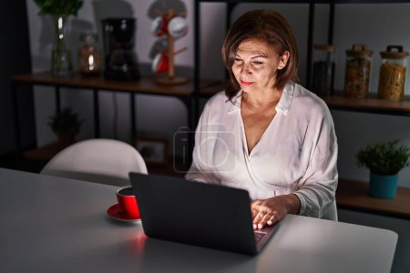 Téléchargez les photos : Femme hispanique du moyen âge en utilisant un ordinateur portable à la maison la nuit déprimé et inquiet pour la détresse, pleurer en colère et peur. triste expression. - en image libre de droit