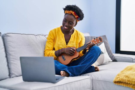 Photo for Young african american woman having online ukelele class sitting on sofa at home - Royalty Free Image
