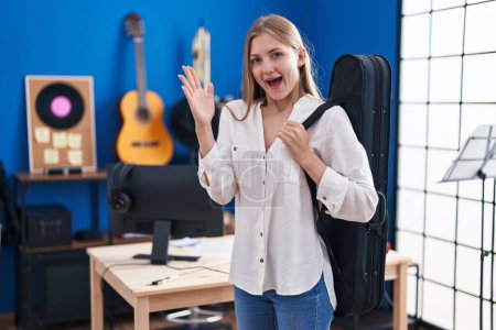 Téléchargez les photos : Jeune femme caucasienne tenant étui de guitare célébrant la victoire avec sourire heureux et expression gagnante avec les mains levées - en image libre de droit