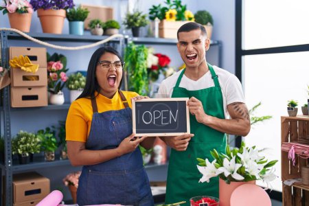 Photo for Young hispanic couple working at florist with open sign angry and mad screaming frustrated and furious, shouting with anger. rage and aggressive concept. - Royalty Free Image