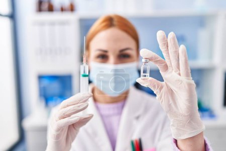 Photo for Young caucasian woman scientist wearing medical mask holding covid vaccine at laboratory - Royalty Free Image