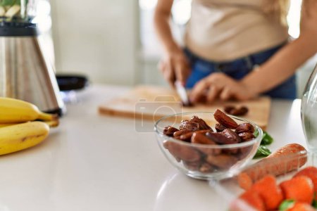 Téléchargez les photos : Jeune belle femme hispanique préparant smoothie aux légumes avec date de coupe mélangeur à la cuisine - en image libre de droit