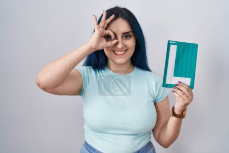 Photo for Young modern girl with blue hair holding l sign for new driver smiling happy doing ok sign with hand on eye looking through fingers - Royalty Free Image