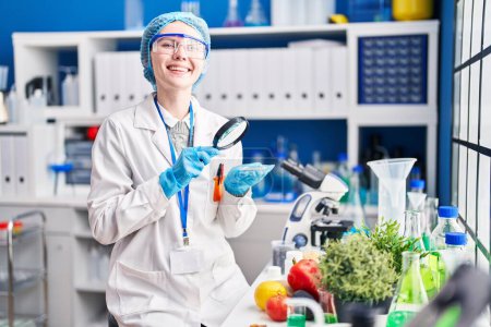 Téléchargez les photos : Jeune femme blonde scientifique à la recherche d'échantillon avec loupe au laboratoire - en image libre de droit