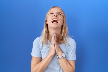 Photo for Young caucasian woman wearing casual blue t shirt begging and praying with hands together with hope expression on face very emotional and worried. begging. - Royalty Free Image