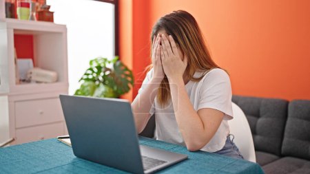 Téléchargez les photos : Jeune femme blonde stressée en utilisant un ordinateur portable à la salle à manger - en image libre de droit