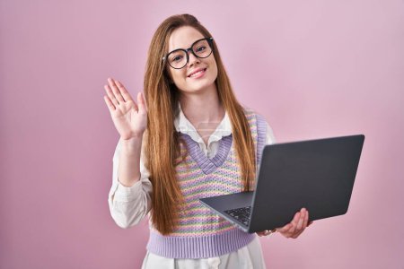 Photo for Young caucasian woman working using computer laptop waiving saying hello happy and smiling, friendly welcome gesture - Royalty Free Image