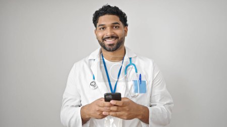 Téléchargez les photos : Afro-Américain homme médecin souriant en utilisant smartphone sur fond blanc isolé - en image libre de droit