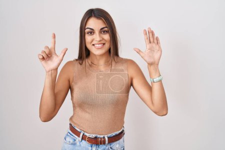 Foto de Mujer hispana joven de pie sobre fondo blanco mostrando y señalando hacia arriba con los dedos número siete mientras sonríe confiado y feliz. - Imagen libre de derechos