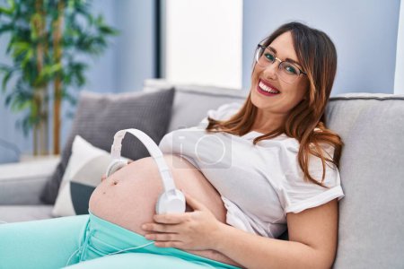 Photo for Young pregnant woman smiling confident putting music to baby at home - Royalty Free Image