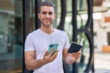 Téléchargez les photos : Jeune homme caucasien utilisant smartphone tenant passeport à la rue - en image libre de droit