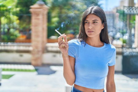Téléchargez les photos : Young beautiful hispanic woman smoking at street - en image libre de droit