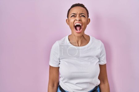 Téléchargez les photos : Belle femme afro-américaine debout sur fond rose en colère et folle hurlant frustrée et furieuse, criant de colère. rage et concept agressif. - en image libre de droit