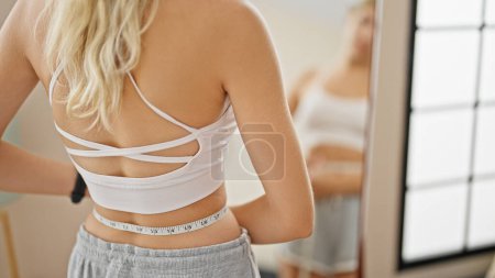 Photo for Young blonde woman measuring waist looking on mirror at home - Royalty Free Image