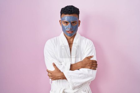 Téléchargez les photos : Jeune homme hispanique portant un masque de beauté et un peignoir de bain tremblant et gelant pour le froid hivernal avec une expression triste et choquante sur le visage - en image libre de droit