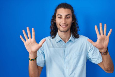 Téléchargez les photos : Young hispanic man standing over blue background showing and pointing up with fingers number ten while smiling confident and happy. - en image libre de droit