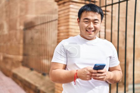 Photo for Young chinese man smiling confident using smartphone at street - Royalty Free Image