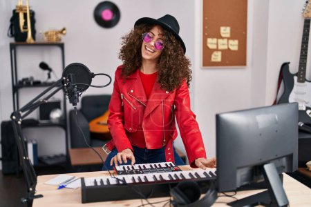 Foto de Joven mujer hispana músico cantando canción tocando el piano en el estudio de música - Imagen libre de derechos