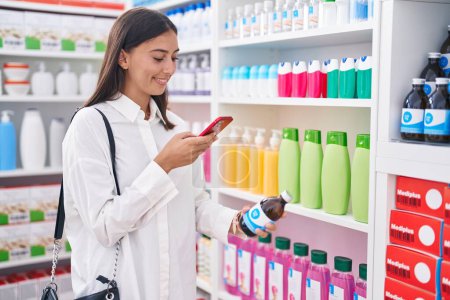 Photo for Young beautiful hispanic woman customer make phot by smartphone to medicine bottle at pharmacy - Royalty Free Image
