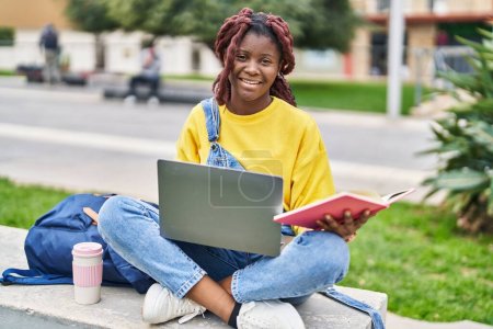 Photo for African american woman student using laptop reading book at campus park - Royalty Free Image