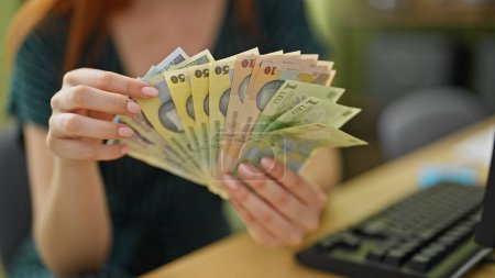 Photo for Young redhead woman business worker counting romanian leu banknotes at office - Royalty Free Image